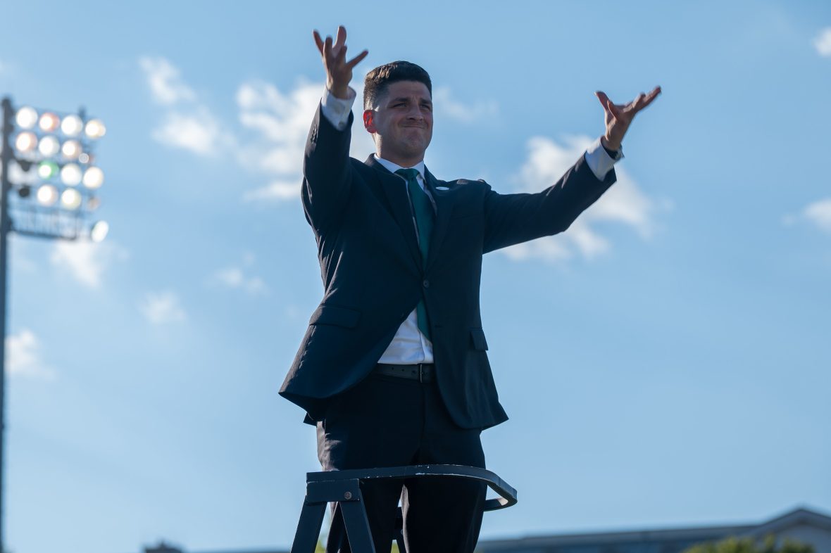 Director of Athletics Bands Brian Taylor conducting, blue sky behind him